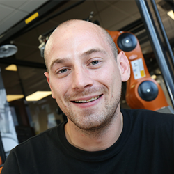 Portrait of Paul Harrold in front of a KUKA robot