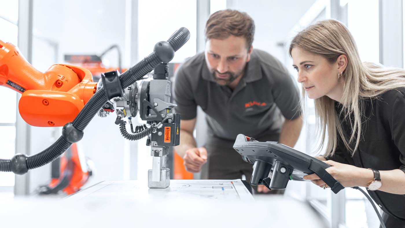 KUKA Mitarbeiter und Kundin mit Steuerger?t am Roboter