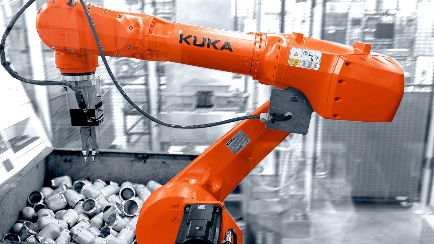 Das Bild zeigt einen orangefarbenen KUKA-Industrieroboterarm in einer automatisierten Fabrik, der ein Metallteil h?lt und die Integration von künstlicher Intelligenz und Automatisierung durch KUKA.SmartBinPicking verdeutlicht.