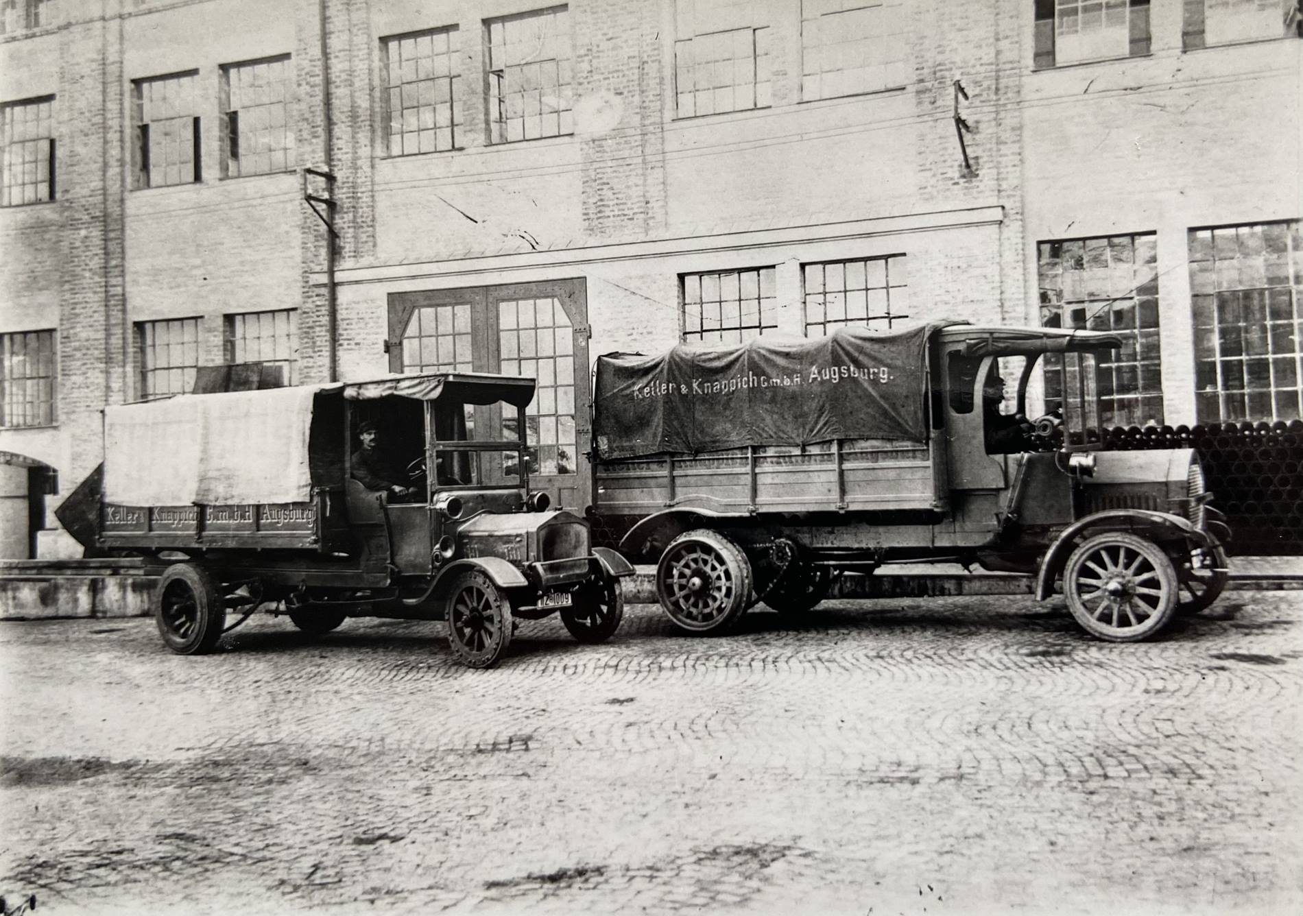Historische LKWs stehen vor einer KUKA Werkshalle: KUKA wird 125 Jahre alt. 